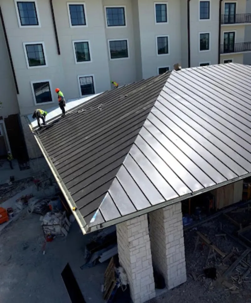 Crew installing standing seam metal roof panels on a commercial project in Ada